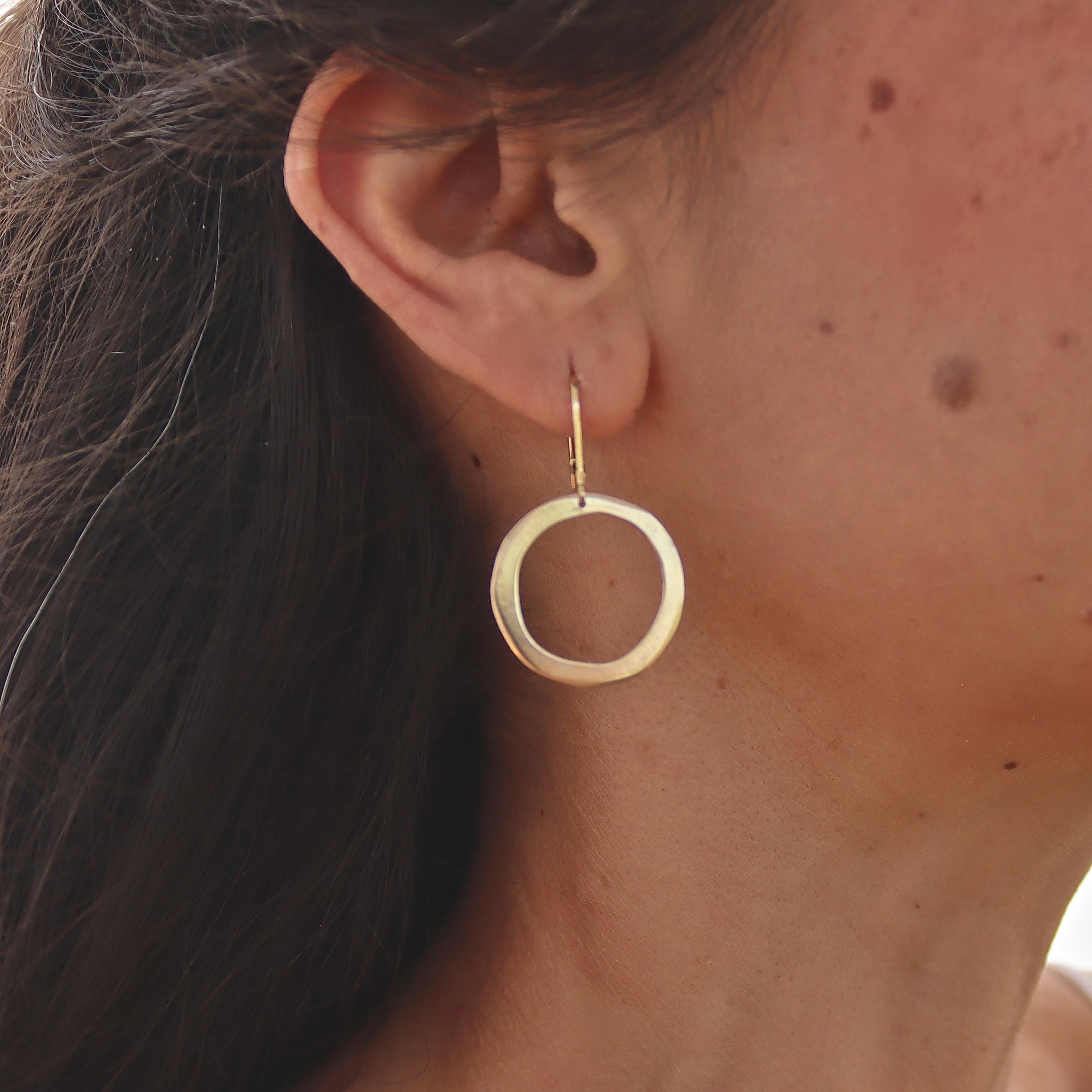 עשוי לכלול: עגילי חישוק זהב בעלי משטח חלק ומעט לא סדיר. החישוקים תלויים על וו פשוט מסוג "סוגר וו".