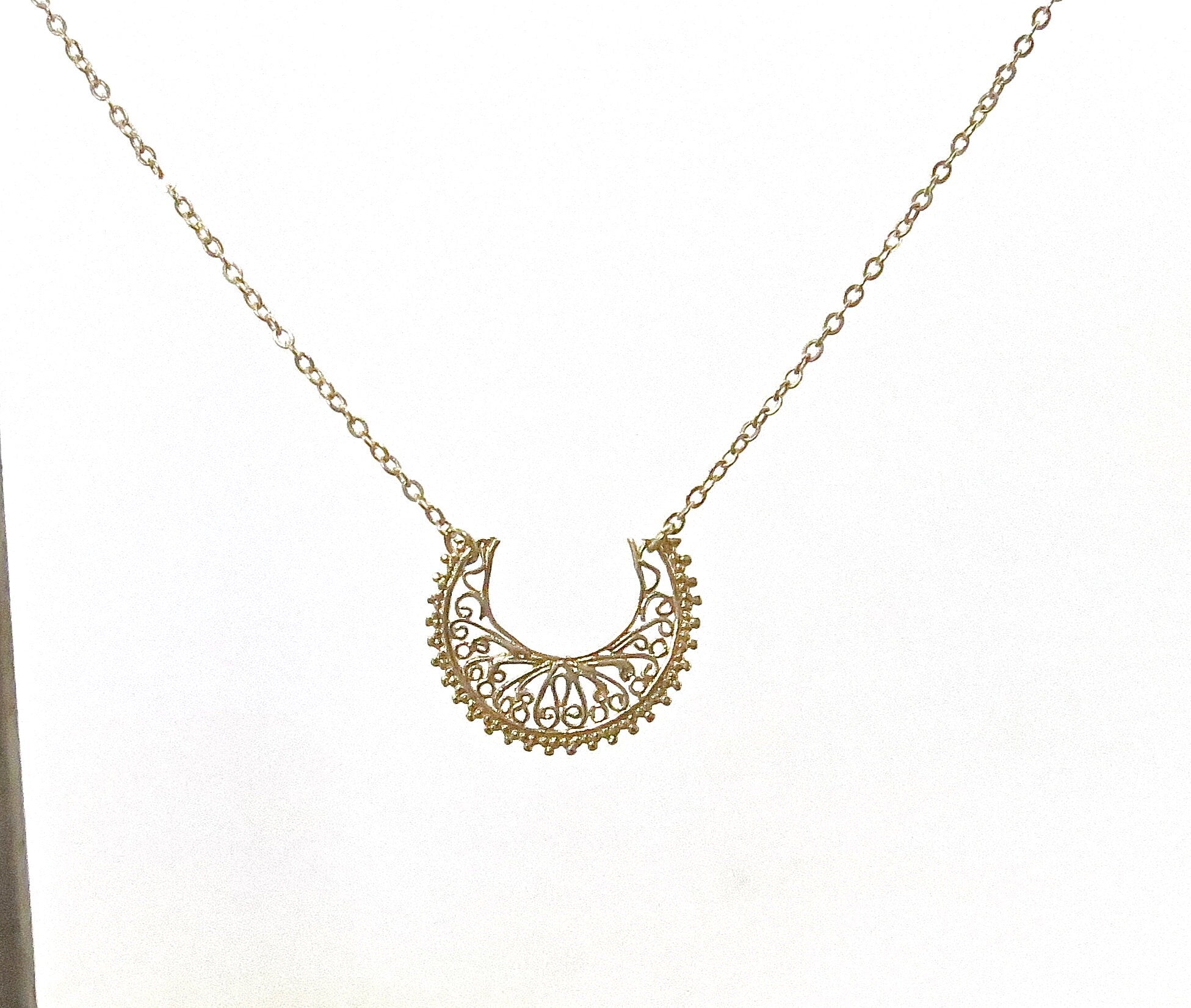 עשוי לכלול: שרשרת סהר זהב עשויה פיליגרן. התליון כולל פרטים מורכבים ועדינים ותלוי על שרשרת זהב משובחת. צורת הסהר מעוטרת בדוגמא פרחונית חוזרת. שרשרת אלגנטית זו מושלמת להוספת נגיעה של קסם בוהמייני לכל תלבושת.