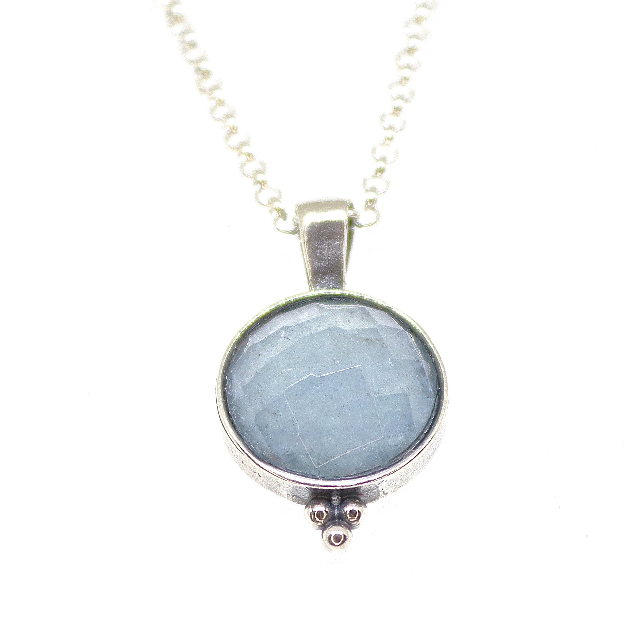 עשוי לכלול: שרשרת כסף עם תליון עגול משובץ באבן חן תכלת. לתליון משטח מחוספס ושלושה חרוזי כסף קטנים בתחתית.