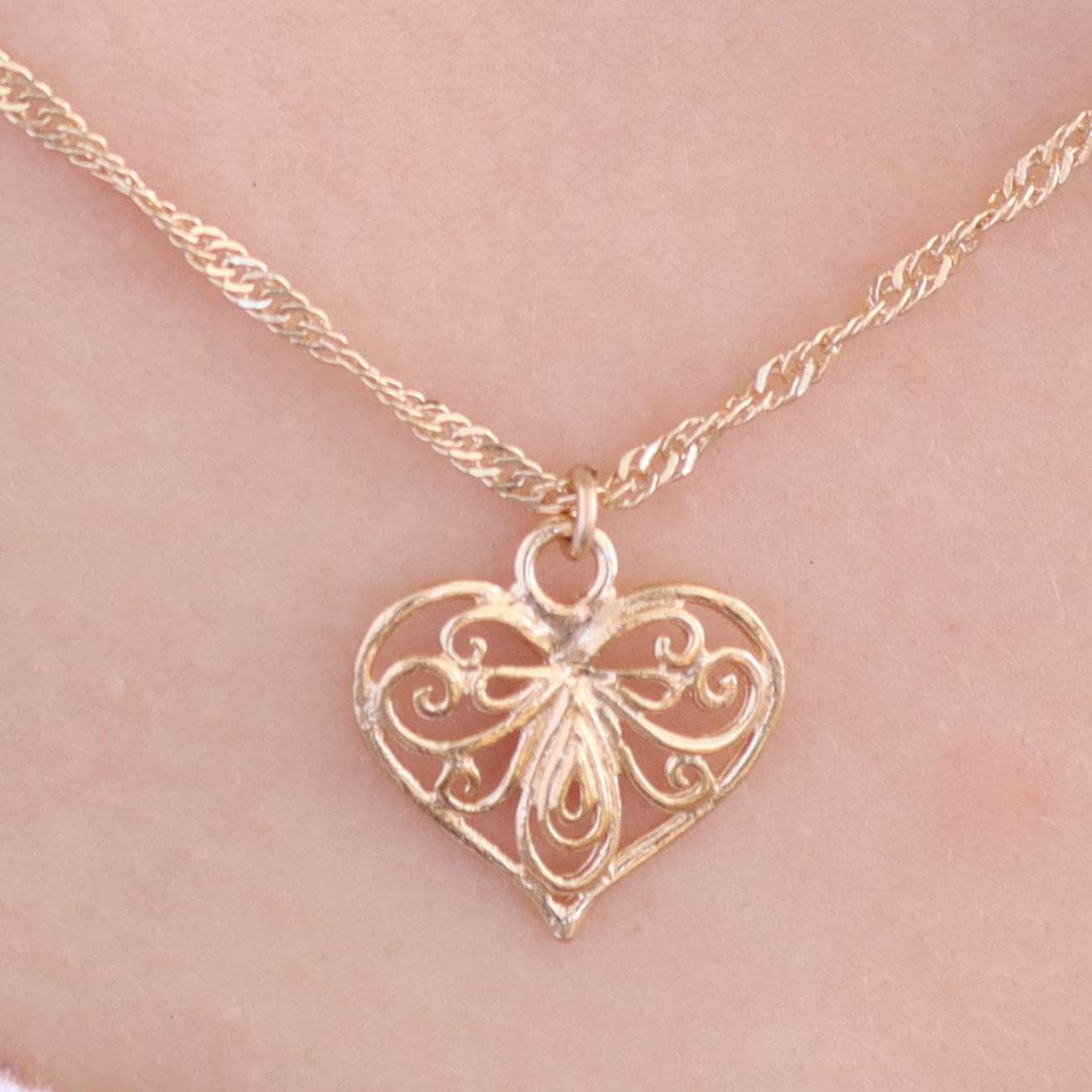 עשוי לכלול: שרשרת תליון זהב בצורת לב עם עיצוב פיליגרן עדין. התליון מחובר לשרשרת זהב דקה.