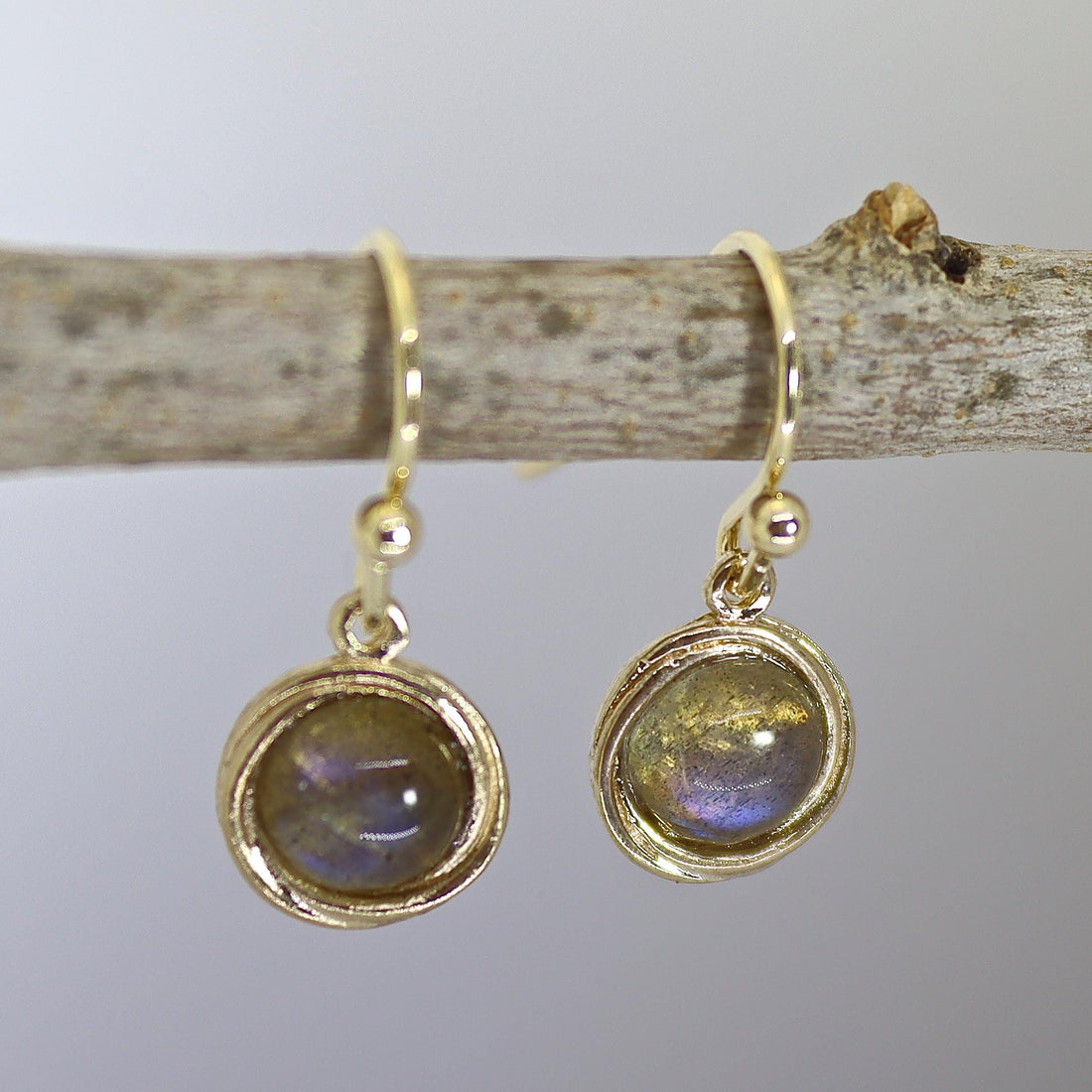 עשוי לכלול: זוג עגילי זהב תלויים עם אבני חן לברדוריט עגולות וססגוניות. לעגילים עיצוב פשוט עם חוט כרוך סביב האבן.