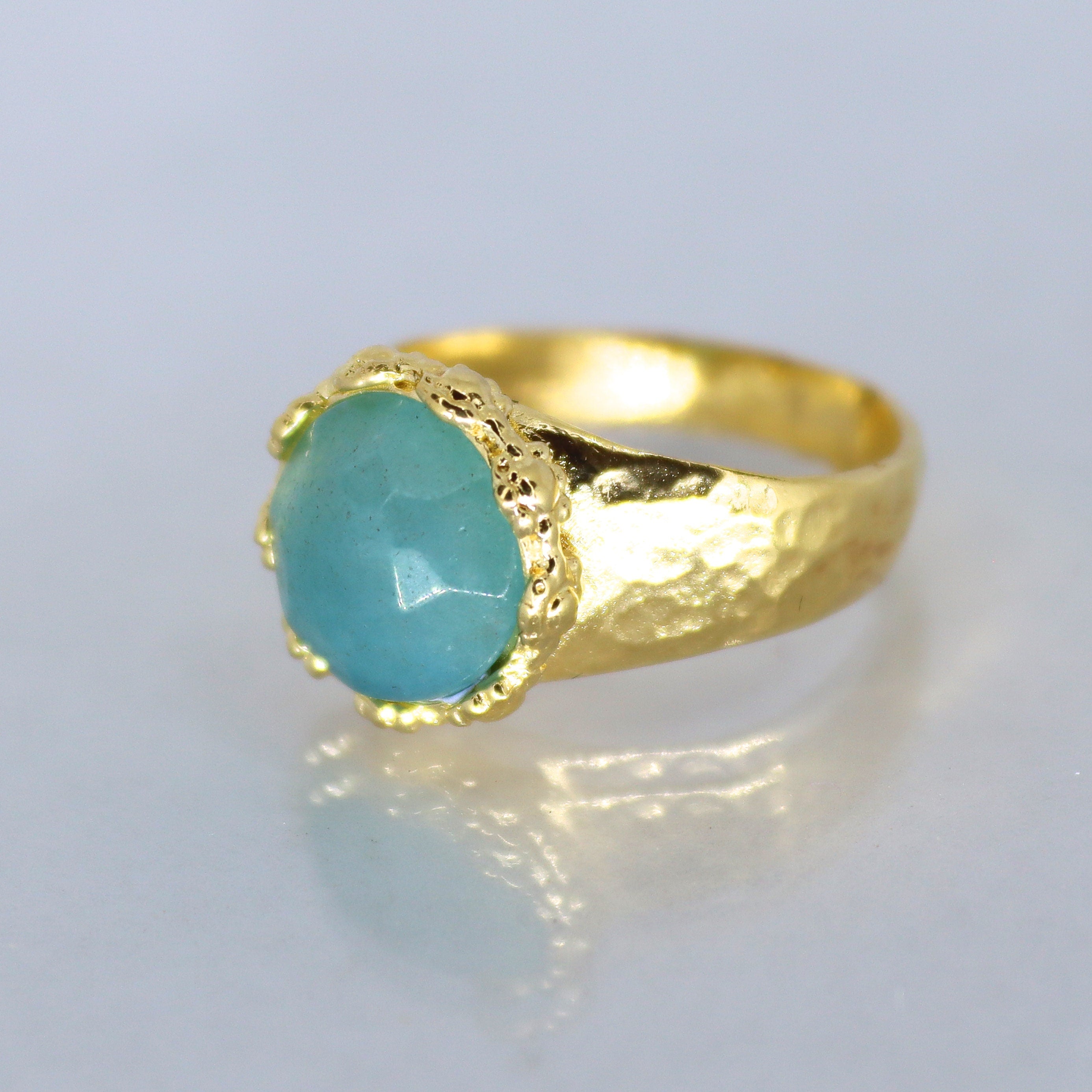 עשוי לכלול: טבעת זהב עם אבן חן אליפטית בצבע תכלת משובצת במסגרת זהב מחוספסת. טבעת הטבעת מחוספסת וכוללת גימור מרוקע.