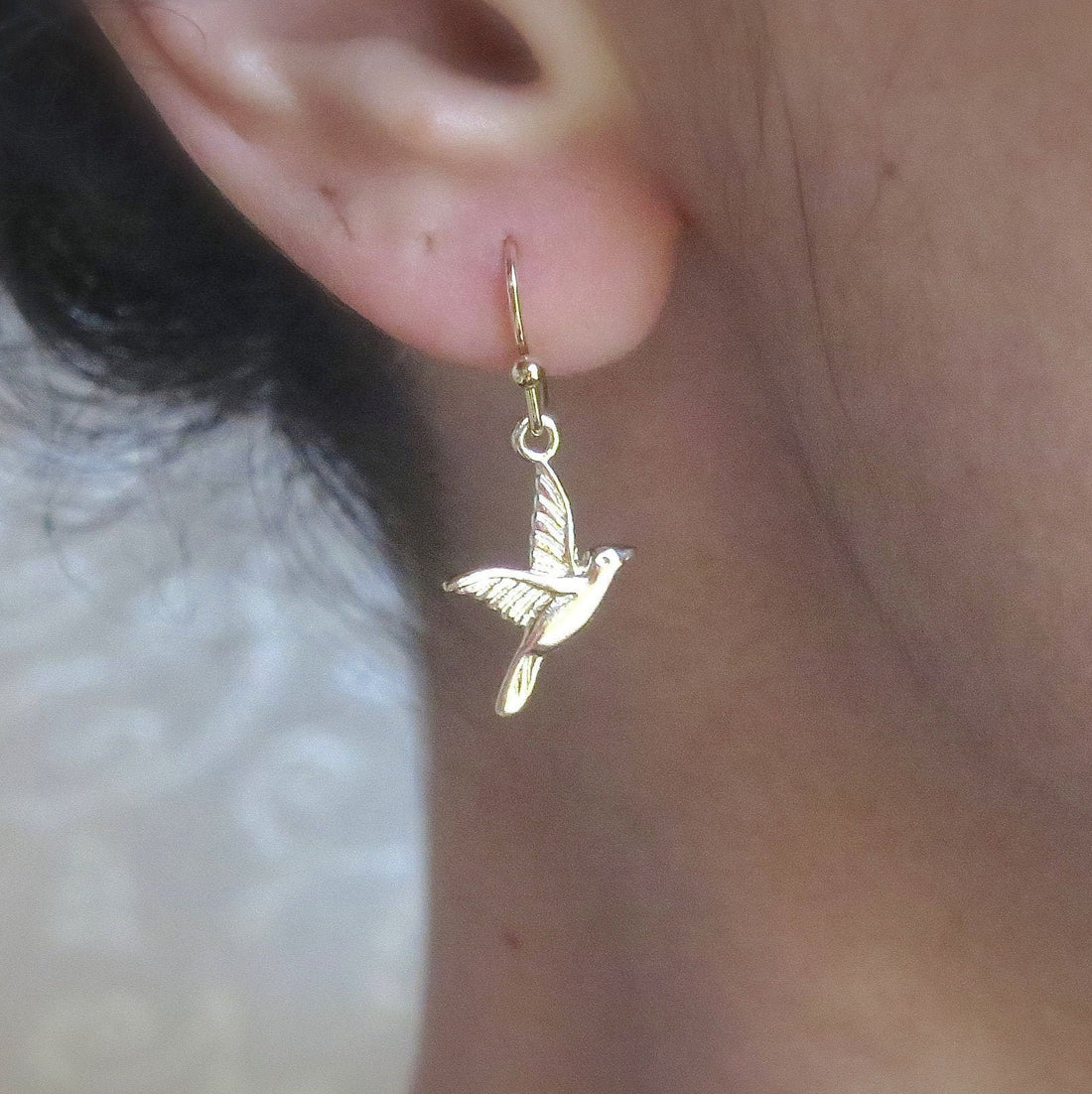 עשוי לכלול: עגילי זהב תלויים בצורת ציפור בעיצוב פשוט. העגילים תלויים מאוזן של אדם.