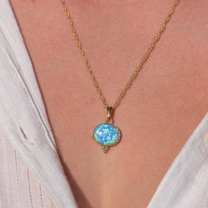 עשוי לכלול: שרשרת זהב עם תליון אופל תכלת. התליון בצורת אליפסה ובעל גבול זהב.