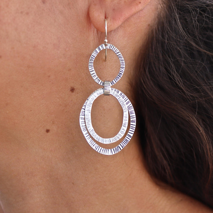 עשוי לכלול: עגילי כסף כפולים עם עיגולים משובצים בגימור טקסטורה.