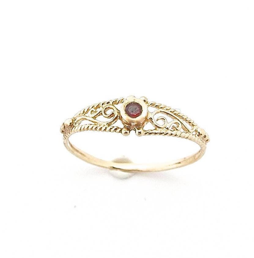 עשוי לכלול: טבעת זהב עדינה עם אבן חן אדומה קטנה משובצת בעיצוב פיליגרן.