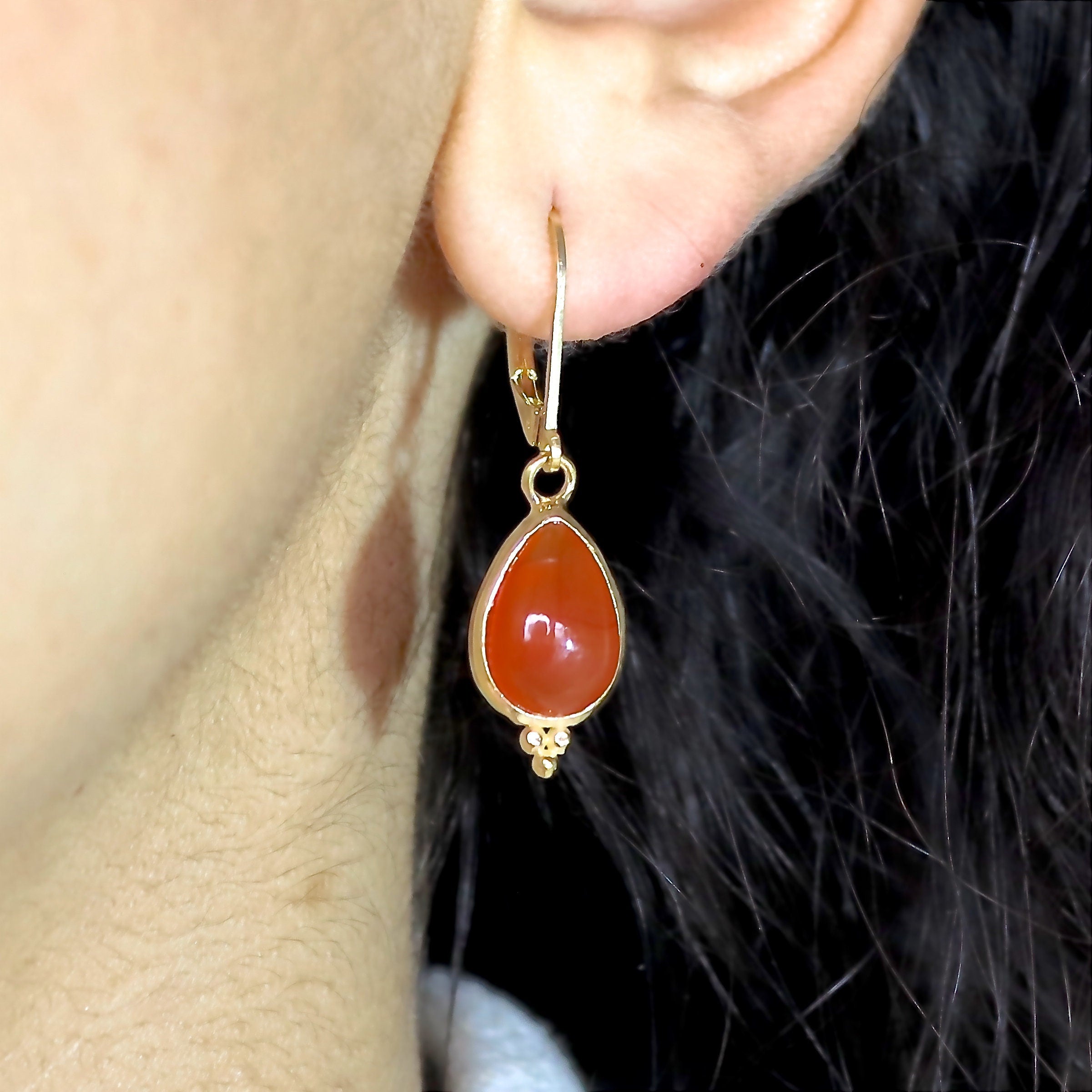 עשוי לכלול: עגילי זהב תלויים בצורת קרנליאן בצורת דמעה. העגילים כוללים אבן חן קרנליאן חלקה ומלוטשת בצורת אגס, משובצת במסגרת זהב. לעגילי הזהב "סוגר חות" יש חרוזים דקורטיביים קטנים מתחת לאבן החן. עגילים אלגנטיים אלה מושלמים להוספת נגיעה של תחכום לכל תלבושת.