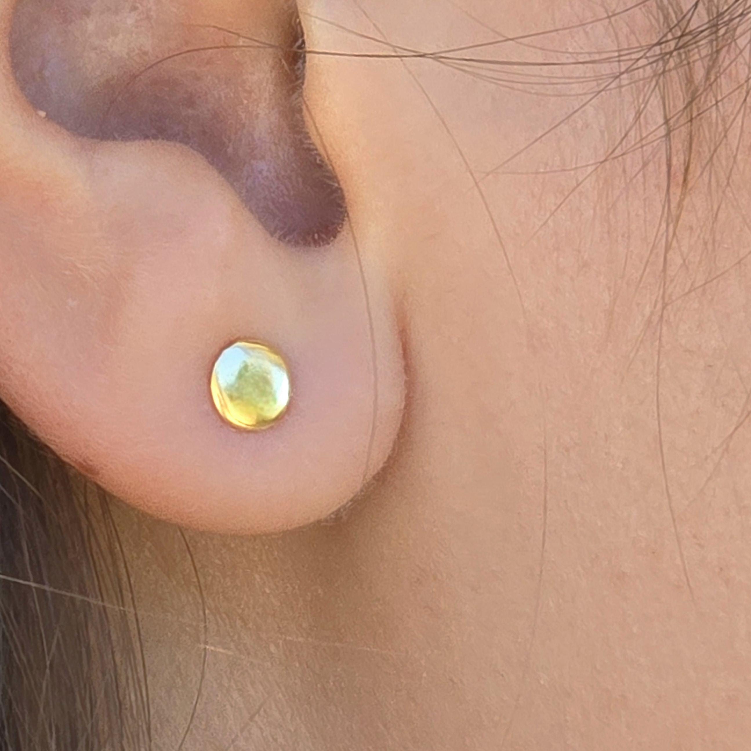 עשוי לכלול: עגיל זהב קטן ועגול מוצג מקרוב. העגיל בצבע זהב אחיד ומבריק ובעל משטח מעט מחוספס. הוא ממוקם על תנוך האוזן, והעור סביב האוזן נראה לעין. העגיל נראה בסגנון עגילי סט.