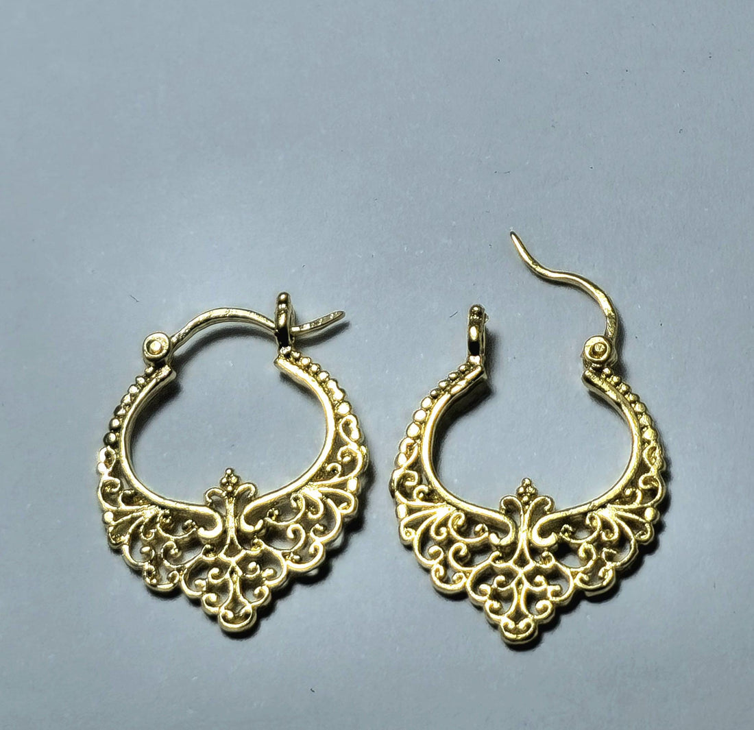 עשוי לכלול: זוג עגילי חישוק בצבע פיליגרן זהב. לכל עגיל מעוצבת ציר מנגנון סגירה ועיצוב מפורט ופתוח של דוגמאות פרחוניות ומגילות. העגילים מוצגים על רקע אפור ניטרלי, המדגיש את עבודת היד המורכבת והגוון המתכתי החם שלהם.