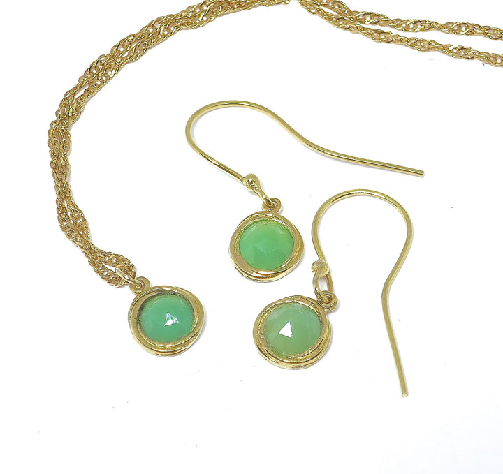 עשוי לכלול: שרשרת ועגילים מזהב משובצים באבני חן עגולות בצבע ירוק בהיר. לשרשרת שרשרת עדינה ומפותלת, והעגילים הם בסגנון טיפה פשוט. האבנים נראות בחיתוך קבושון ובעלות איכות עדינה ושקופה. התכשיטים אלגנטיים ומינימליסטיים, מתאימים לענידה יומיומית או לאירועים מיוחדים. הזהב הוא בגוון צהוב חם.