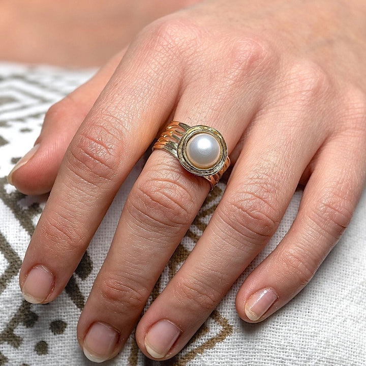 עשוי לכלול: טבעת זהב עם פנינה לבנה משובצת במסגרת עגולה. לטבעת רצועה בעלת טקסטורה.