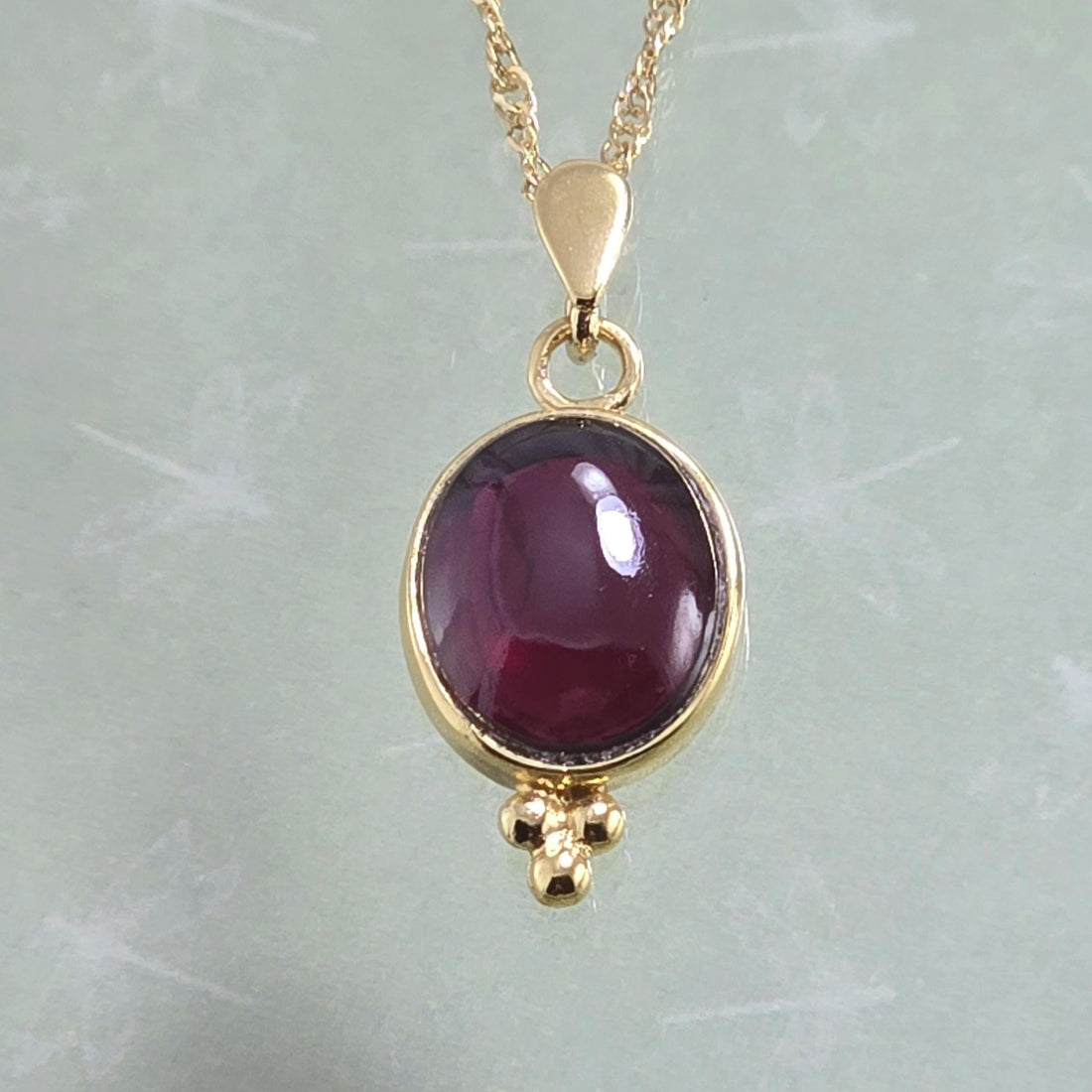 עשוי לכלול: שרשרת תליון זהב הכוללת אבן חן גדולה, בצורת אליפסה, אדומה עמוקה. אבן החן משובצת במסגרת זהב והיא נקודת המוקד. לתליון לולאת זהב קטנה לשרשרת ואשכול של שלושה חרוזי זהב בתחתית. השרשרת היא שרשרת כבלים עדינה עשויה זהב.